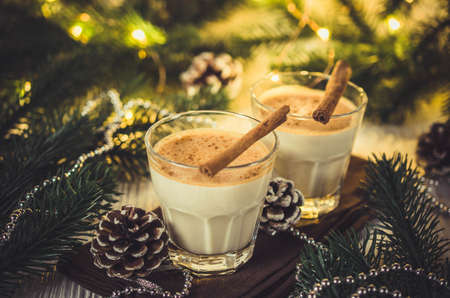 Christmas Traditional Homemade Eggnog in Festive Atmosphere. Fir branches with Christmas Lights and Decorations. Milk Cocktail with Spice. Selective Focus. Copy Space.の写真素材