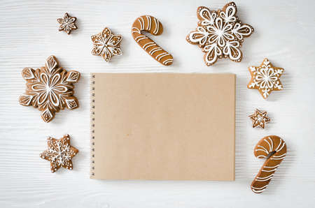 Christmas gingerbread on white wooden table. Brown notebook for writing recipe or cover cookbook. Culinary background. Top view with copy space.の写真素材