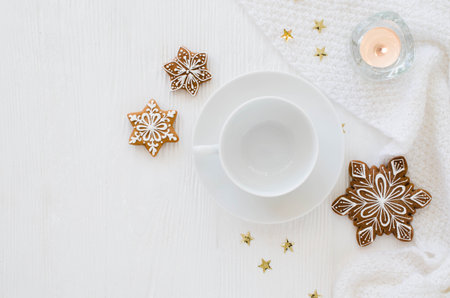 Christmas background. Empty white cup, gingerbread, candles and knitted scarf on a white wooden...