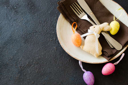 Festive table setting for holiday Easter dinner on dark table. Decorative rabbit and colorful eggs. Copy spaceの写真素材