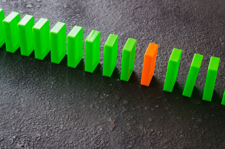 Domino effect - row of green dominoes on dark background. The concept of a weak link.