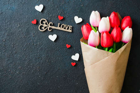 Holiday background with spring flowers. Bouquet of tulips and decorative key on dark background. Greeting card for Valentine's, Women's or Mother's day. Flat lay, top view, copy spaceの写真素材