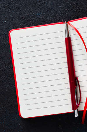 Empty red notebook with red pen on dark background. Blank paper for text. Flat lay, top view, copy spaceの写真素材