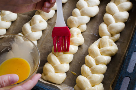 Preparation process - raw unbaked buns. Female hand lubricates raw buns with an egg before baking....