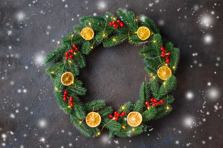Christmas door wreath made of tree fir branches with xmas lights and decorations on dark background. Copy space in center frame and empty mock up for text.の写真素材