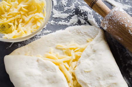 Rolled dough, baking flour, grated cheese and rolling pin on a dark blackboard. Place for text or...