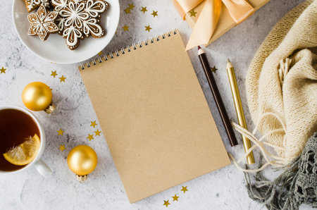 Christmas background with blank brown notebook with gift box, tea, gingerbread cookies and plaid....