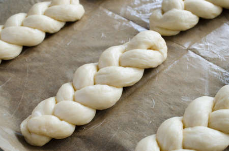 Preparation process - raw unbaked buns. Ready to bake homemade traditional pigtail buns on baking paper. Rustic style. Traditional pastryの写真素材