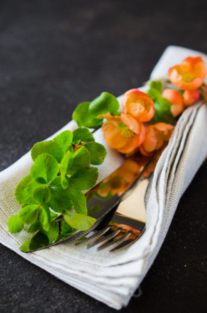 Vintage table setting with delicate flowers on a linen napkin on a dark background, close-up....
