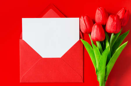 Greeting card for Valentine's Day, Woman's Day or Mother's Day. Red envelope with blank white paper and bouquet of tulips. Top view with space for your text. Flat layの写真素材