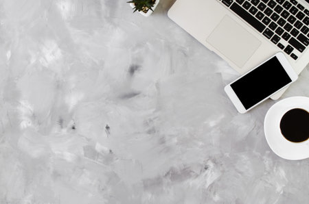 White smartphone with black blank screen on office desk with laptop and cup of coffee on gray...