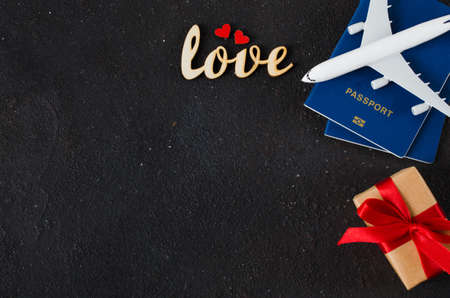 Holiday Travel Planning. Greeting card for Valentine's Day or Woman's Day. Airplane model, passports, bouquet of tulips and gift box on dark background. Top view or flat lay. Copy Space.の写真素材