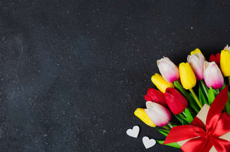 Bouquet of tulips and gift box on dark background. Spring background. Greeting card for Valentine's Day, Woman's Day and Mother's Day. Top view, copy space.の写真素材