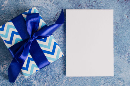 Greeting card for Father's Day or Birthday. Gift box with blank white paper on blue background. Mock...