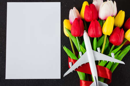 Travel planning on Valentines day. Travel concept, mockup. Blank white paper, bouquet of tulips, gift box and model of passenger plane on dark background. Top view or flat lay. Copy Space.の写真素材