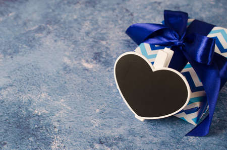 Blue gift box with ribbon. Heart shaped chalkboard with copy space. Classic blue color of the year 2020.の写真素材
