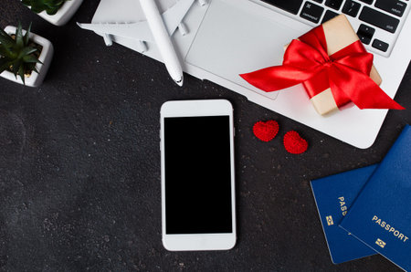 Travel booking concept. Smartphone, airplane model, laptop, passports and gift box on dark...