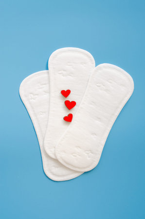 Feminine hygiene pad with red heards on blue background. Imitation of bleeding. Concept of feminine...