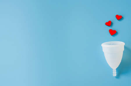 Menstrual cup with red hearts on blue background. Detail of object of intimate hygiene of woman. Imitation of bleeding.の写真素材