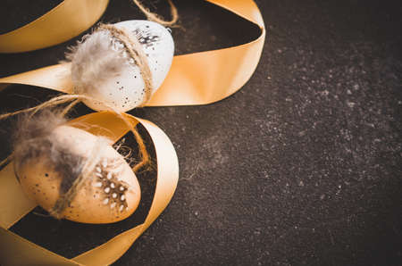Easter background with decorations. Decorative easter eggs with feathers and ribbon on a dark concrete background.の写真素材