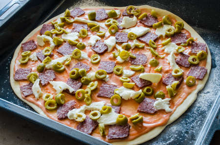 Home made raw pizza with salami, mozzarella, olives and cheese.の写真素材