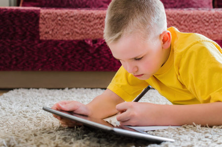 Distance learning online education. Schoolboy studying at home with digital tablet in hand and doing...