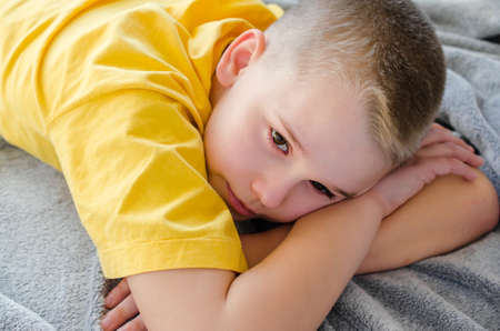 Blond boy dreams or thinks while lying on sofa at home. Rest in daytime. Stay at home. Isolation. Quarantine. Top viewの写真素材