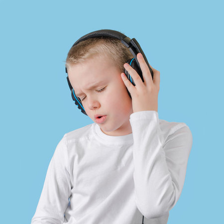 Young child keep your hands on the headphones, enjoying listening to music and sings. Teen boy with...