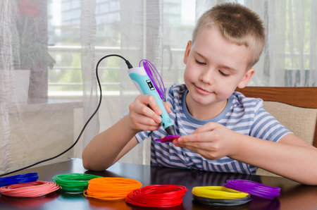 Boy using 3D pen. Happy child making flower from colored ABS plastic. Creative hobby at home,...