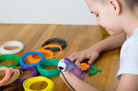 Child using 3D pen. Happy boy making flower from colored ABS plastic. Creative hobby at home,...