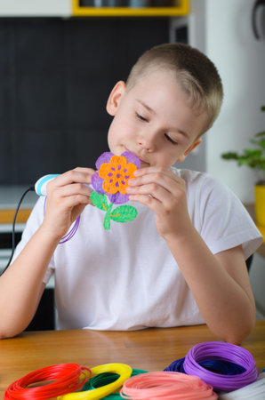 Child using 3D pen. Happy boy making flower from colored ABS plastic. Creative hobby at home, technology, leisure, education concept.の写真素材