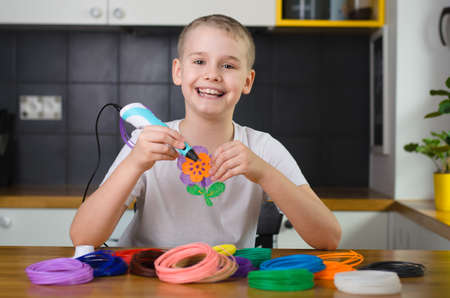 Child using 3D pen. Happy boy making flower from colored ABS plastic. Creative hobby at home, technology, leisure, education concept.の写真素材