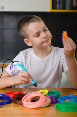 Child using 3D pen. Happy boy making flower from colored ABS plastic. Creative hobby at home, technology, leisure, education concept.の写真素材