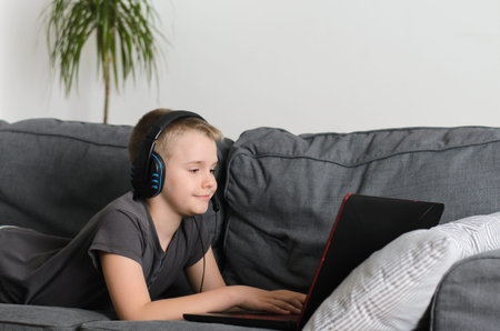 Happy boy in headphones playing or studying on laptop computer at home. Technology concept, gaming...