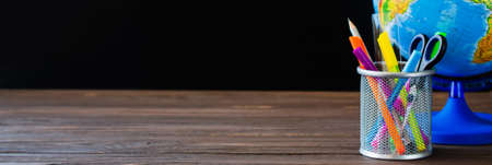 Back to school. School supplies and globe on black board background. Education concept. Copy space. Bannerの写真素材