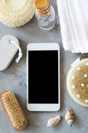 Spa wellness setting concept. Spa accessories and smartphone on gray concrete background. Towel, massage brush, pumice. Flat Lay, top view. Copy spaceの写真素材