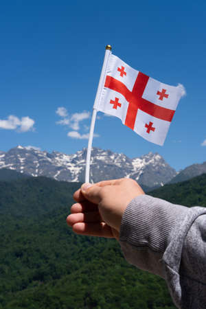Georgian flag in mans hand on Background of Mountains and Blue Sky.の写真素材