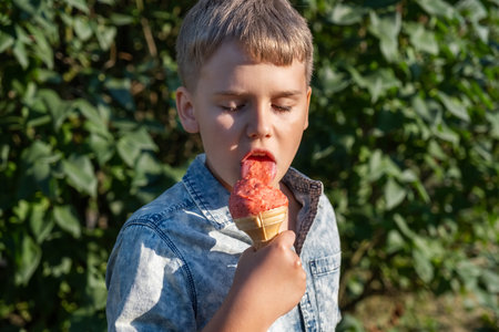 Blond boy eating strawberry ice cream in park on warm sunny summer day.の写真素材