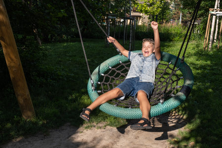 Cute blond boy swinging on a public playground swing.