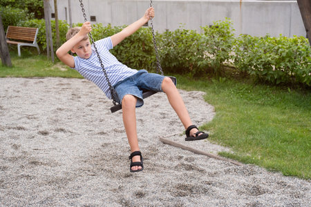 Cute blond boy swinging on a public playground swing.