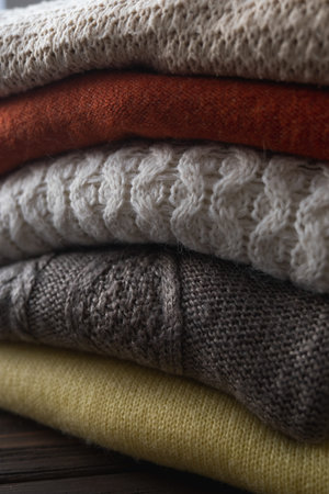 Cozy sweaters in autumn colors on brown wooden background.