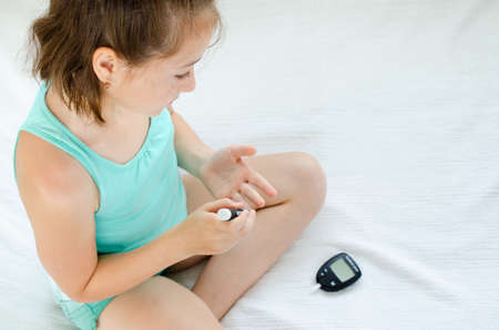 Little girl checking blood sugar level using lancelet and glucometer at home.の写真素材