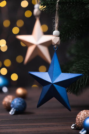Christmas composition with blue and beige stars, fir tree branches on blurred brown background.