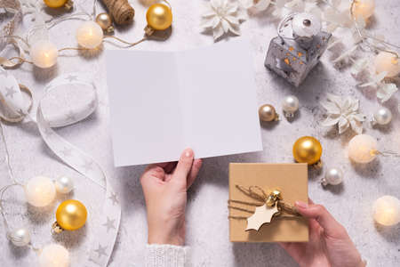 Christmas composition, female hands hold empty postcard and present. Christmas decoration in whiteの写真素材