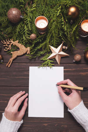 Female hands write Christmas postcard or wishlist on wooden background.の写真素材