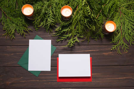 Christmas letters with empty cards lie on a brown wooden table with fir branches and candles.の写真素材