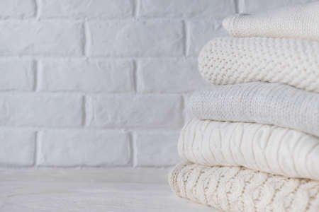 Stack of white cozy knitted sweaters against the background of white brick wall.の写真素材
