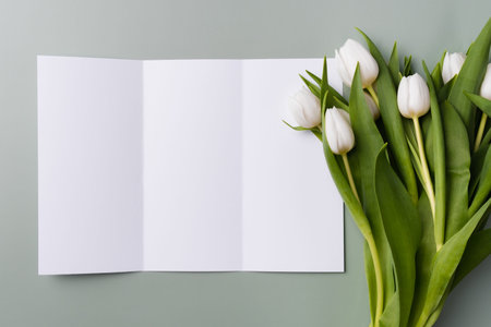 White mockup of trifold brochure on a pale green background with a bouquet of white beautiful...