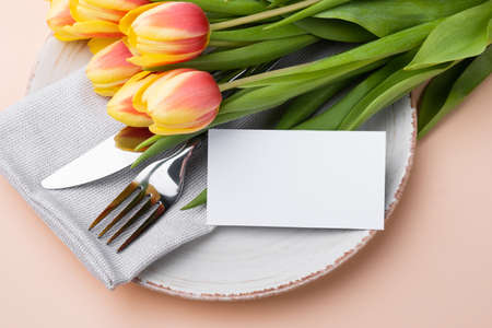 Festive table setting with a card and bouquet of tulips on a beige background. Mockupの写真素材