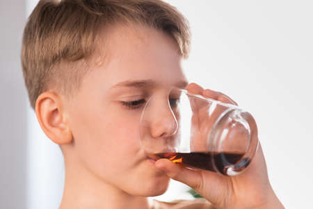 Blond teenager boy drinks cola  at home. Portrait of a cute schoolboyの写真素材